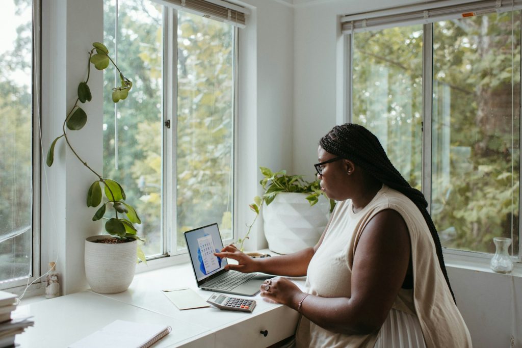 a woman sitting at a table with a laptop in a quiet corner of a room with ample light